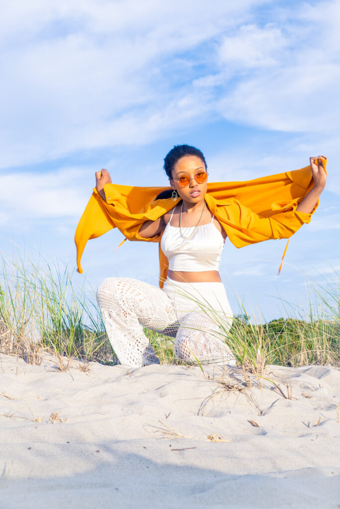 Woman on beach with orange jacket and white pants/top