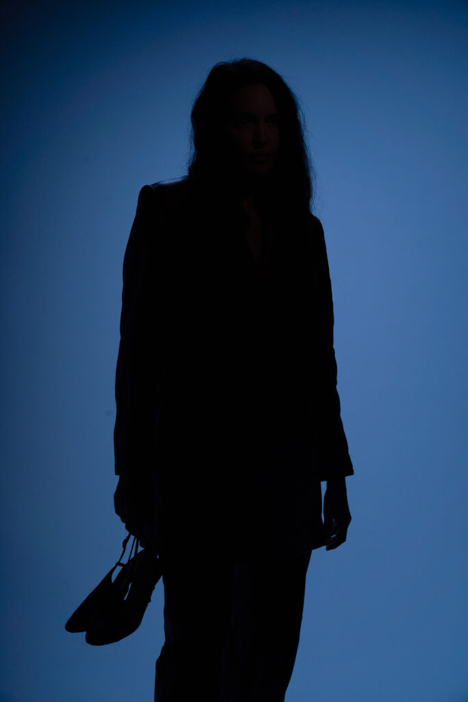Silhouette of woman holding shoes against a dark blue background